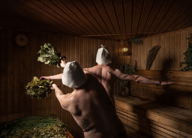 Saunující se finové s metličkami v saunovacích čepicích